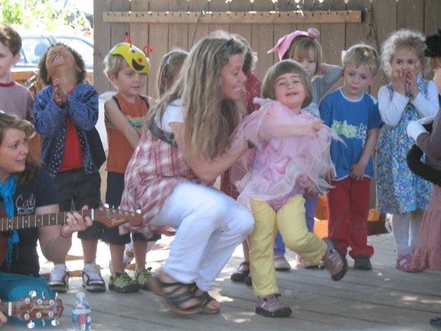 Adult and children gathered, one adult playing guitar, another adult with a child