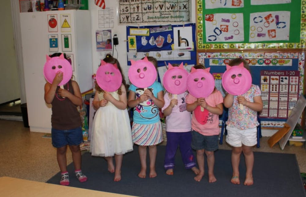 Children holding pink pig masks in front of their faces in a classroom