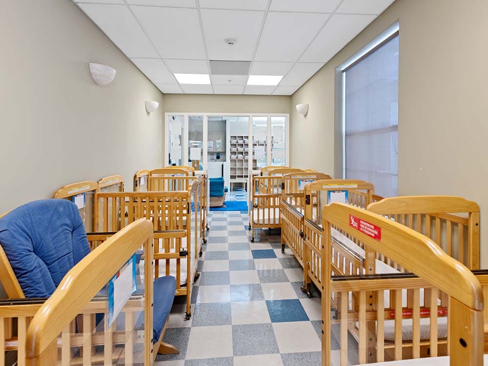 Rows of wooden cribs in a daycare room with a checkered floor