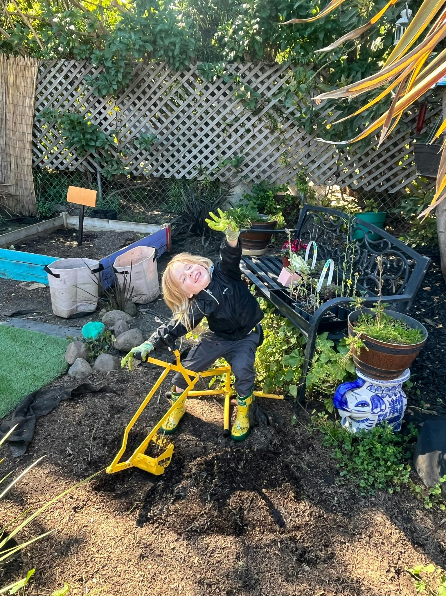 Child in yellow boots and gloves playing with a toy digger in dirt