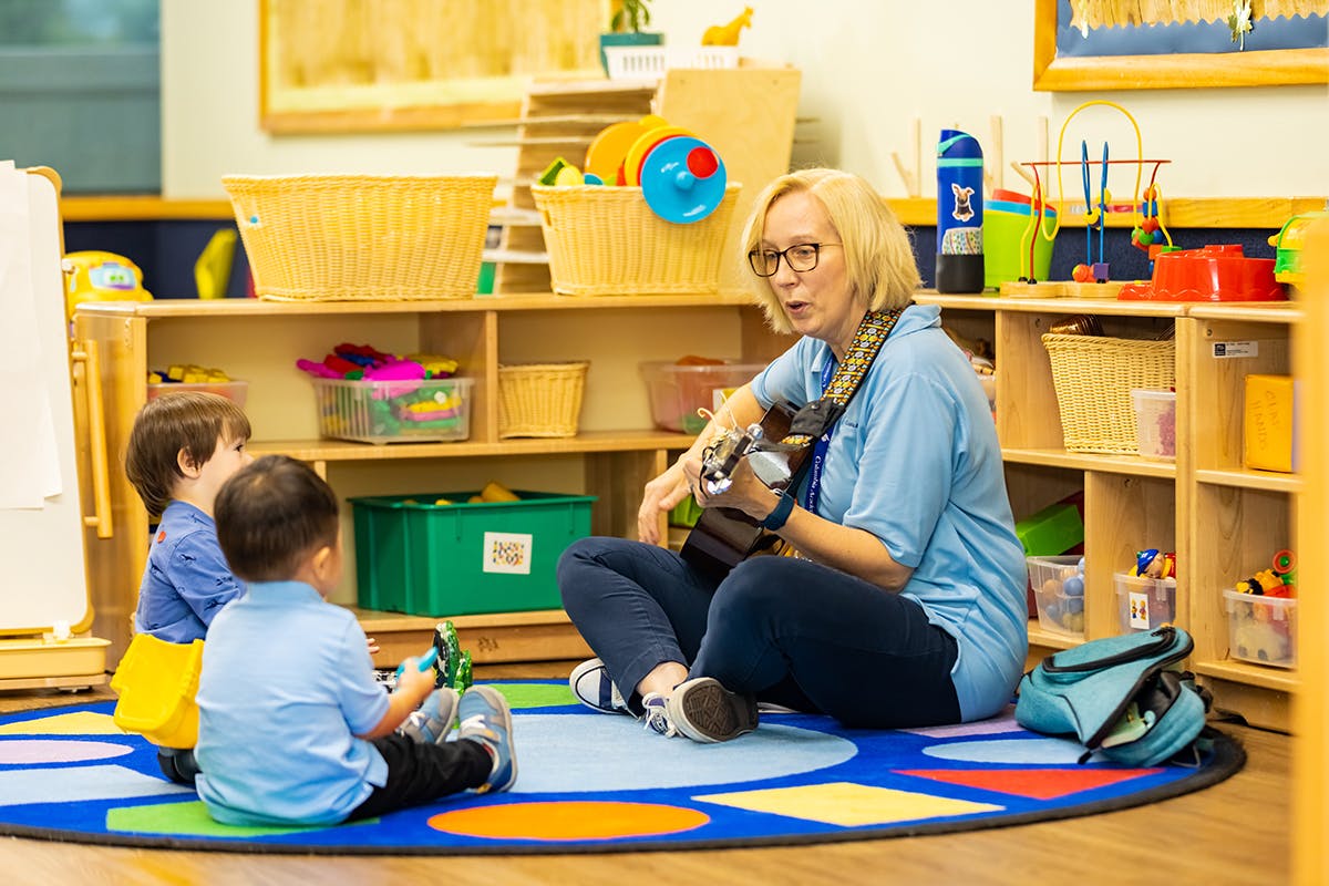 Person playing guitar for two children in a classroom