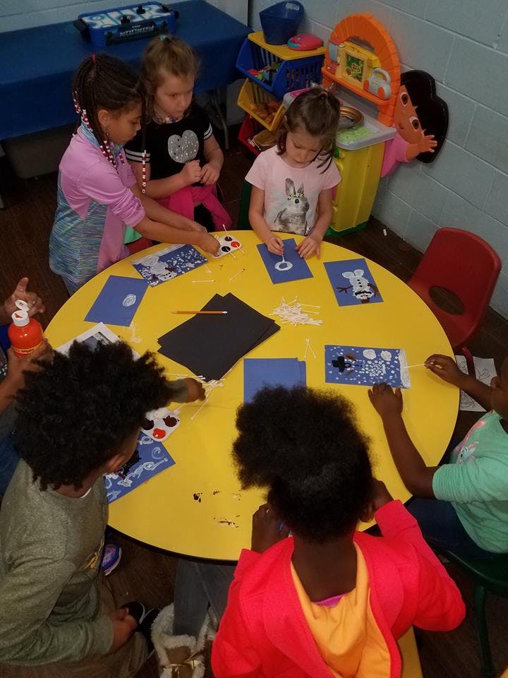 Children gathered around a yellow table doing crafts