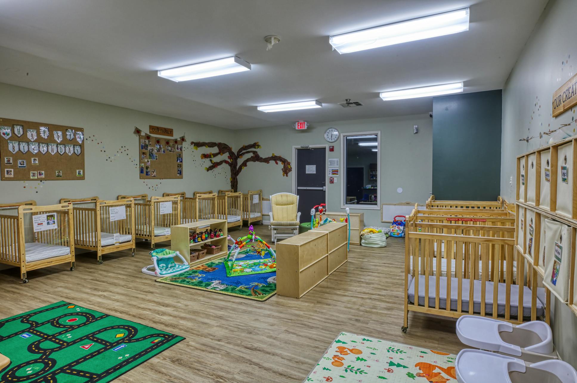 A brightly lit nursery with many cribs and colorful rugs on the floor