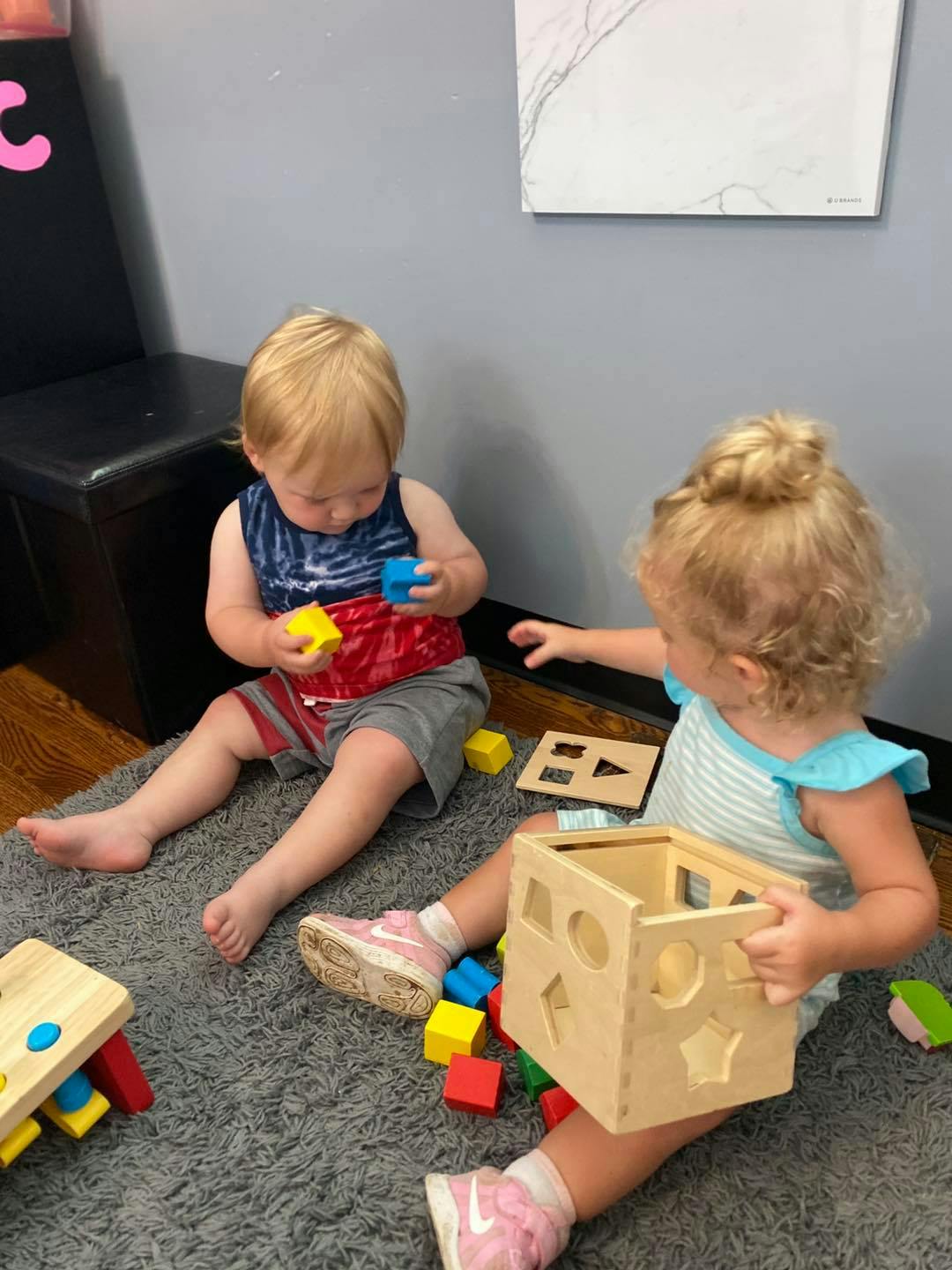 Two children playing with shape sorters and blocks on a rug