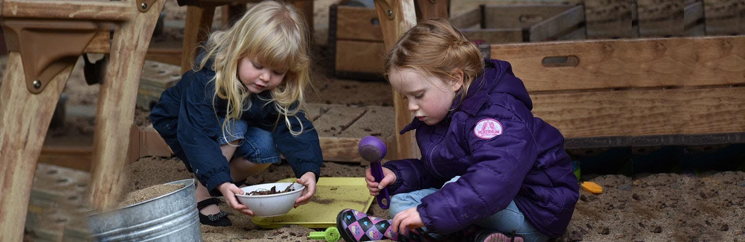 Two children playing in dirt with a bowl and a toy