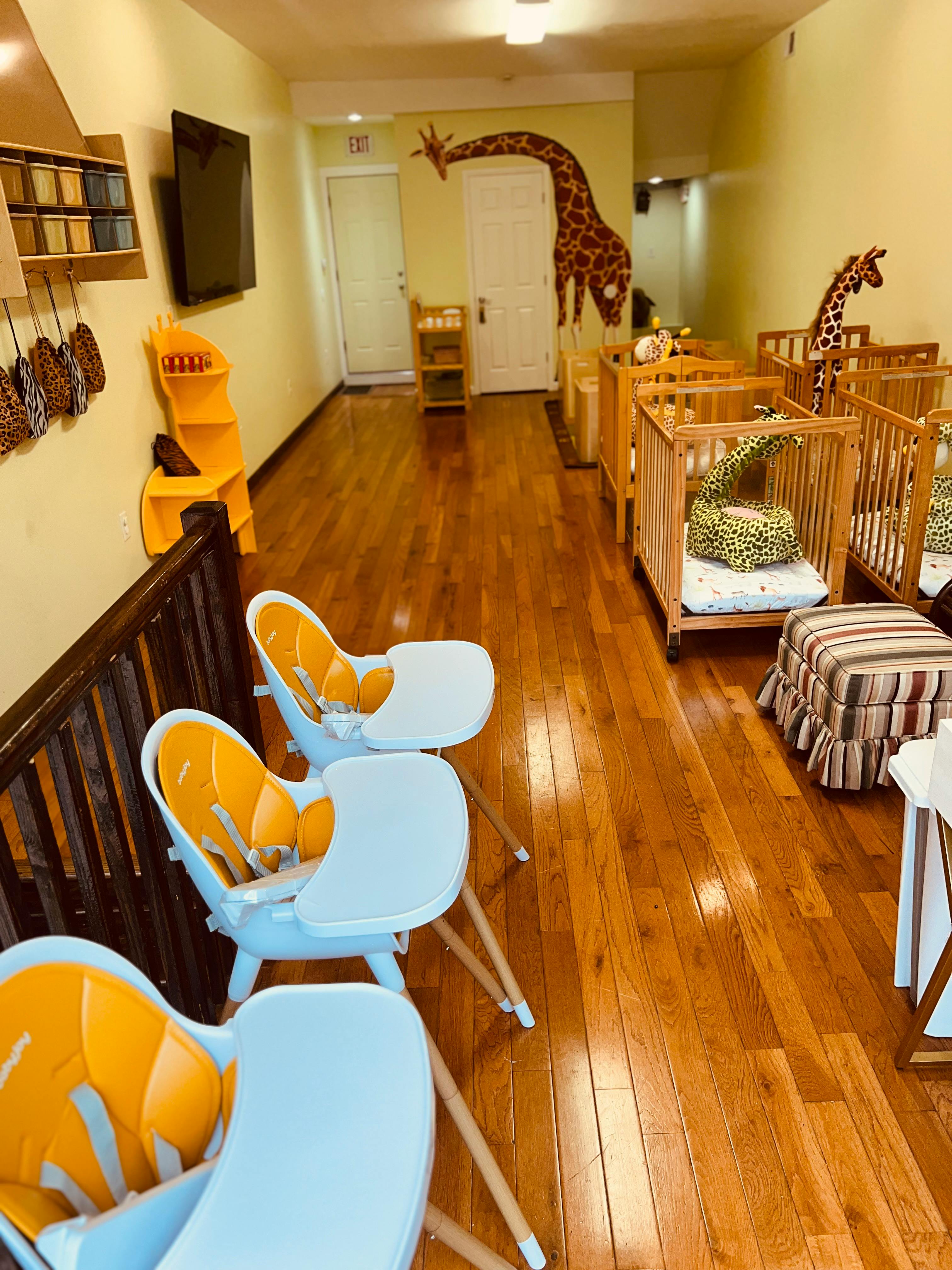 High chairs and cribs in a room with giraffe wall decals