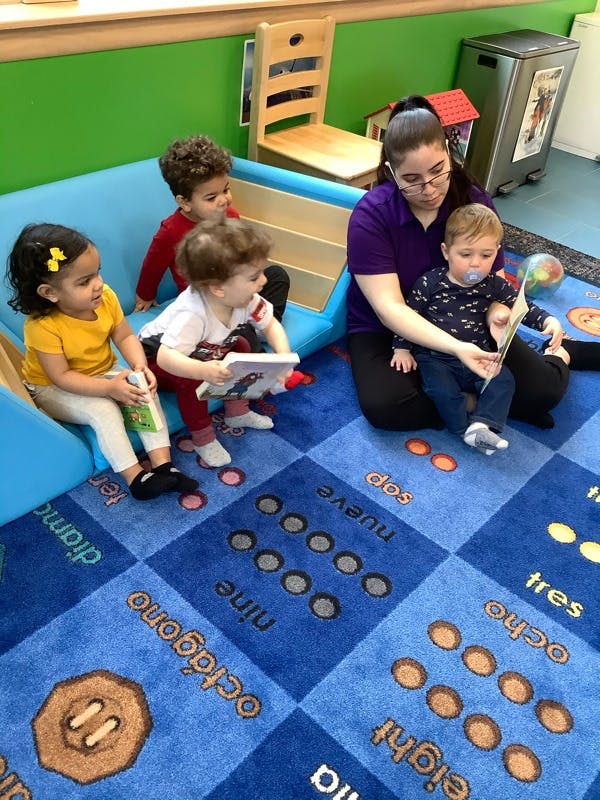 Adult and four children sitting on a blue rug with numbers and shapes