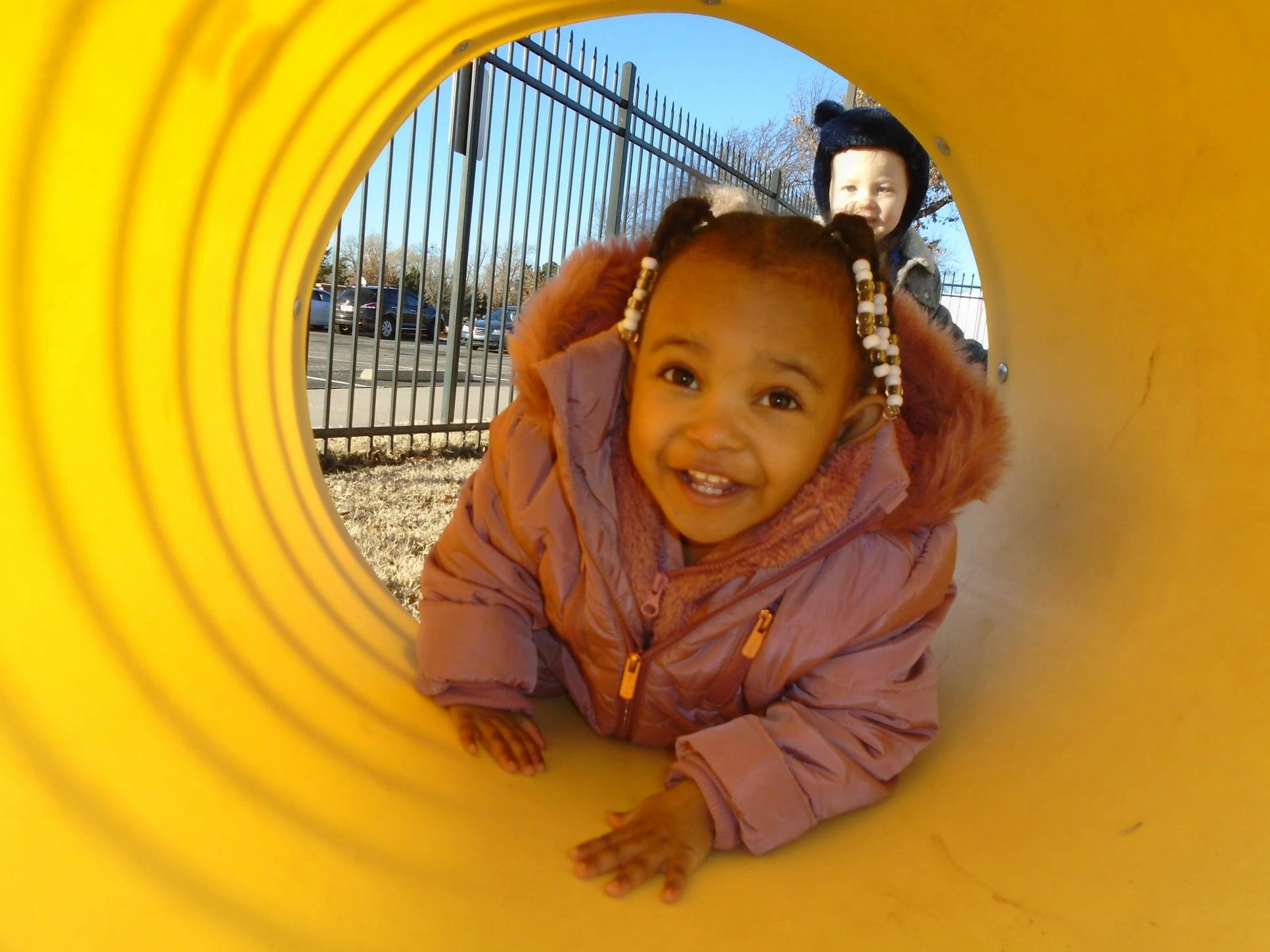 Child crawling through a yellow tunnel, another child in background