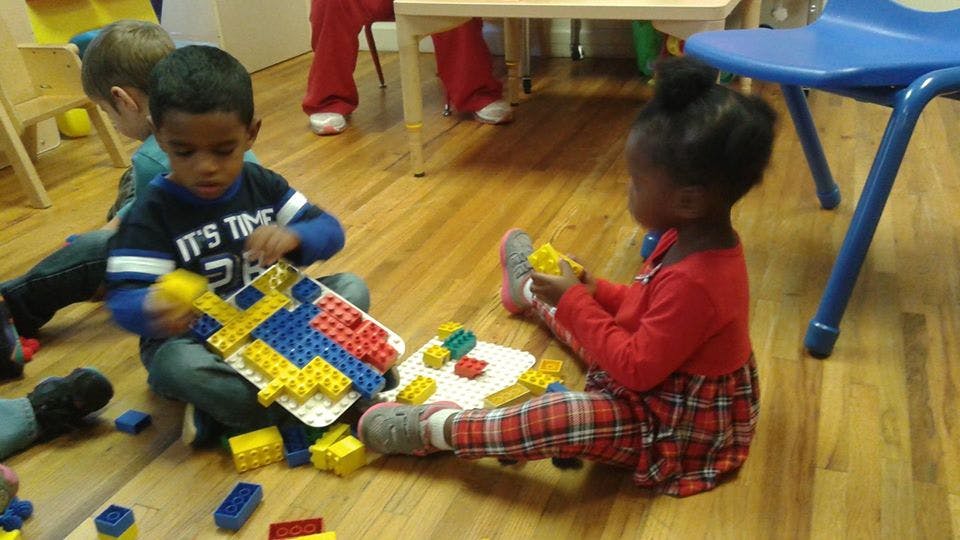 Two children playing with colorful building blocks on a wooden floor