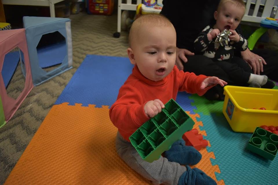 Child in red shirt holding a green toy on a playmat