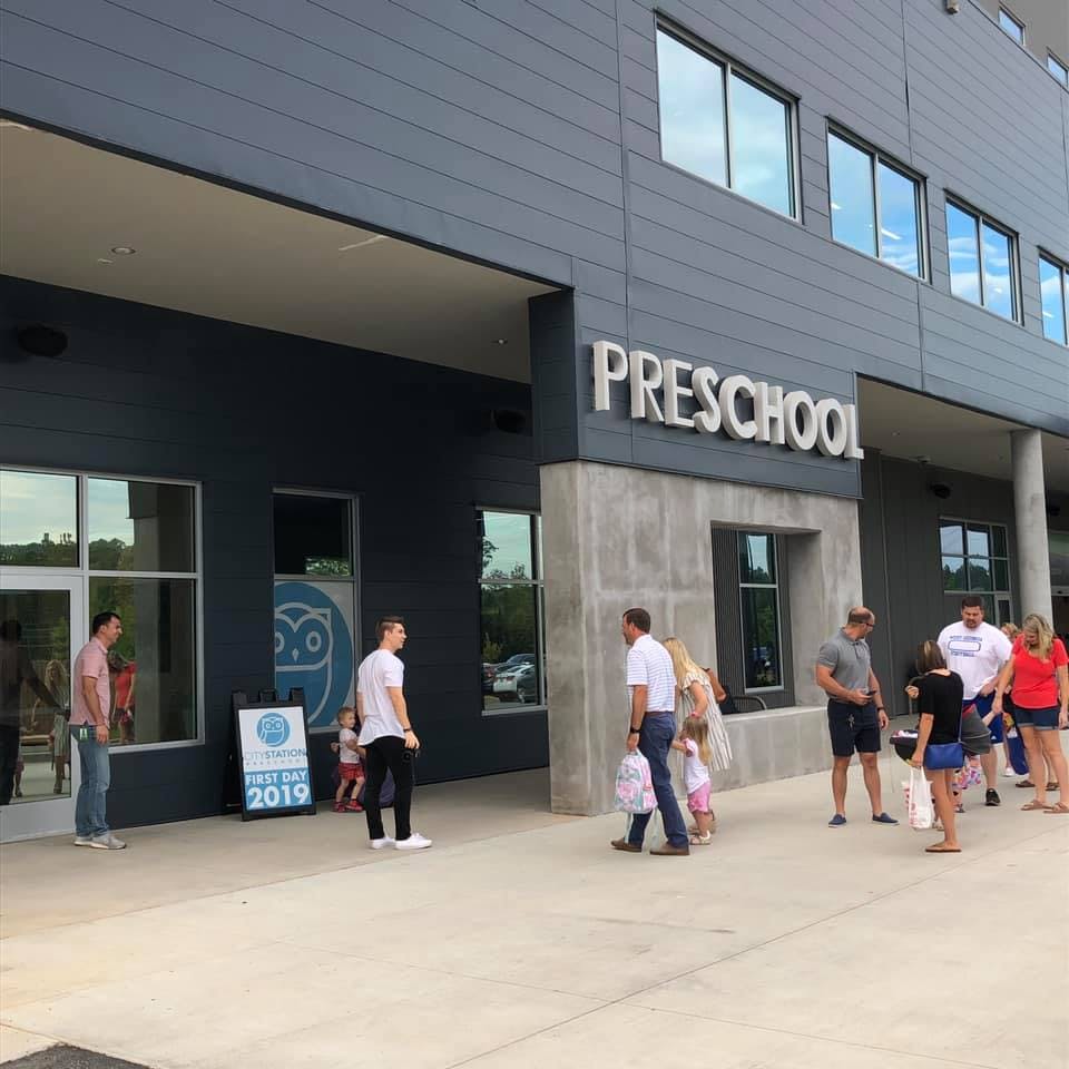 People and children outside a building with a "PRESCHOOL" sign