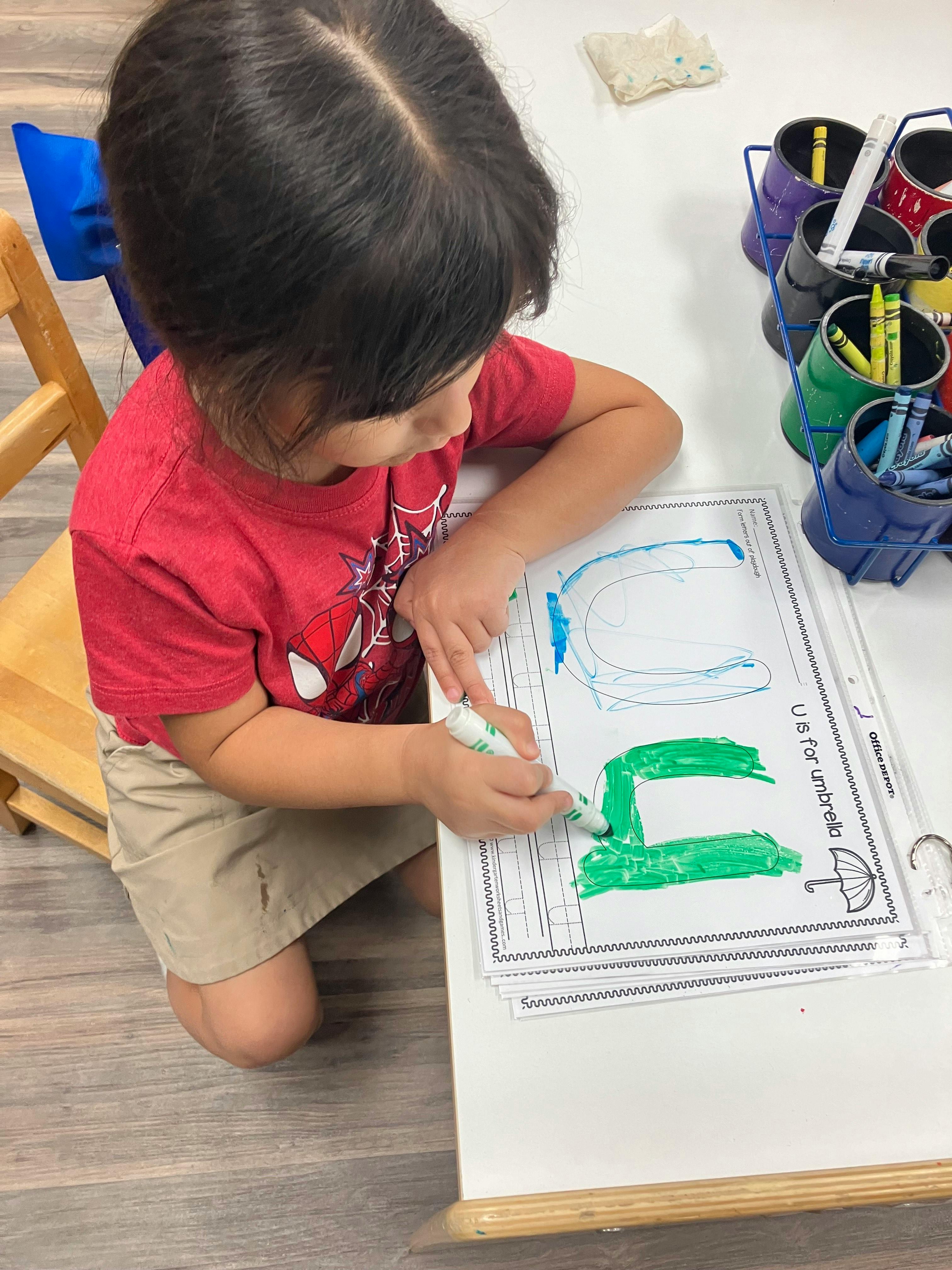 Child coloring a letter U on a worksheet