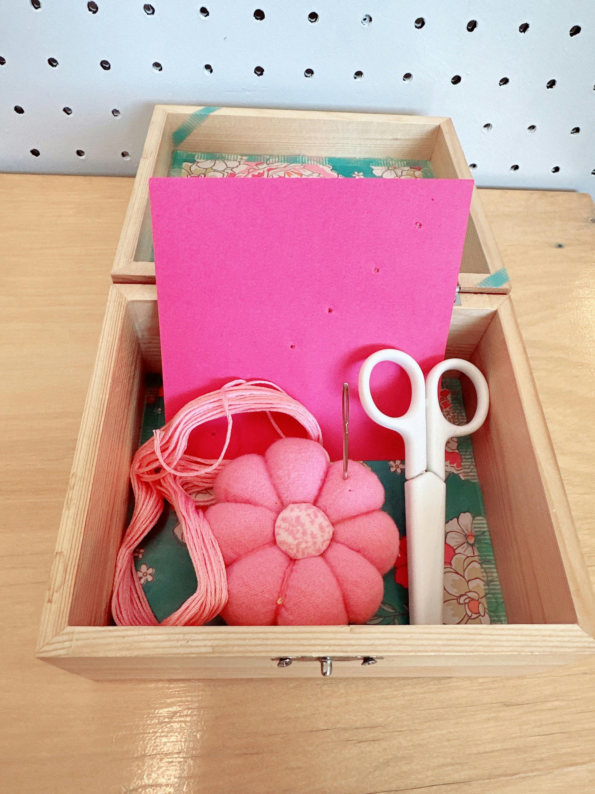 Wooden box containing embroidery floss, a flower pin cushion, needle, and scissors