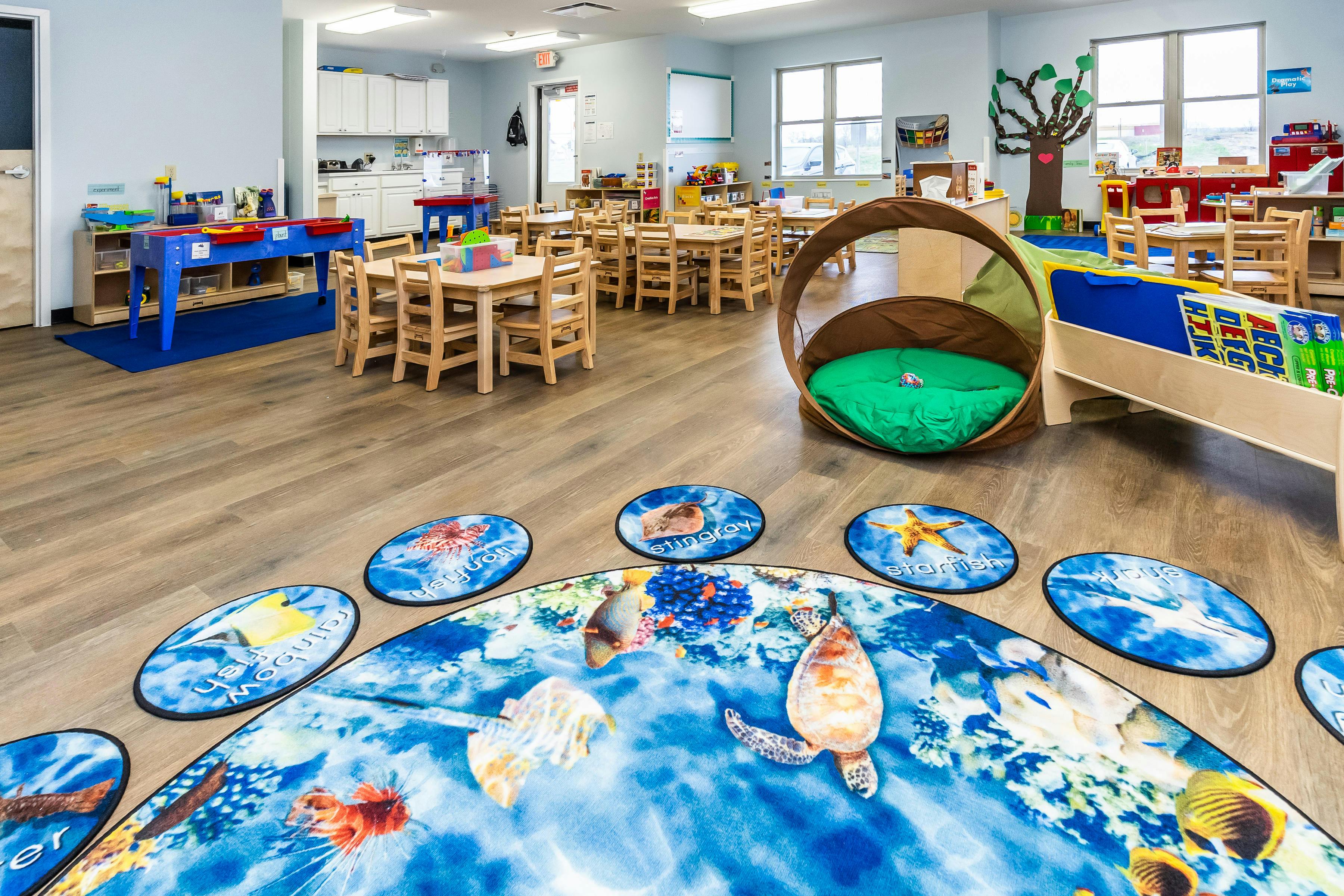 A colorful early childhood classroom with activity tables, chairs, and play areas