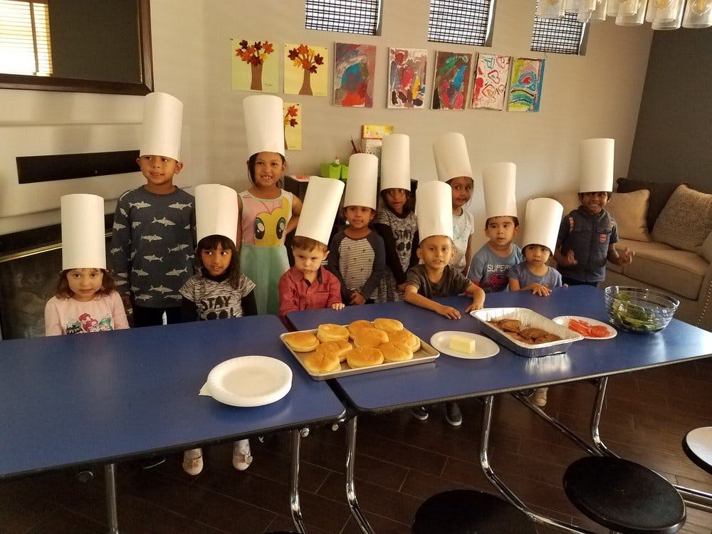 Children wearing chef hats standing behind a table with food