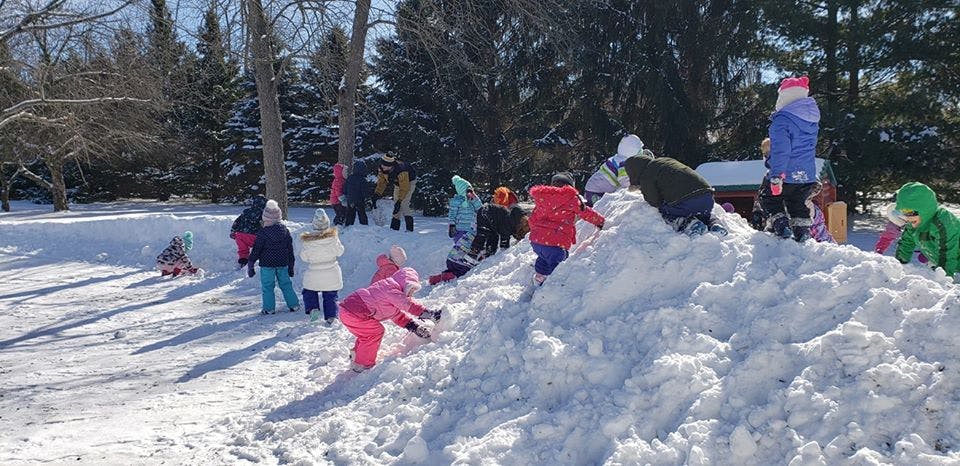 Children playing in snow, some climbing a snow pile