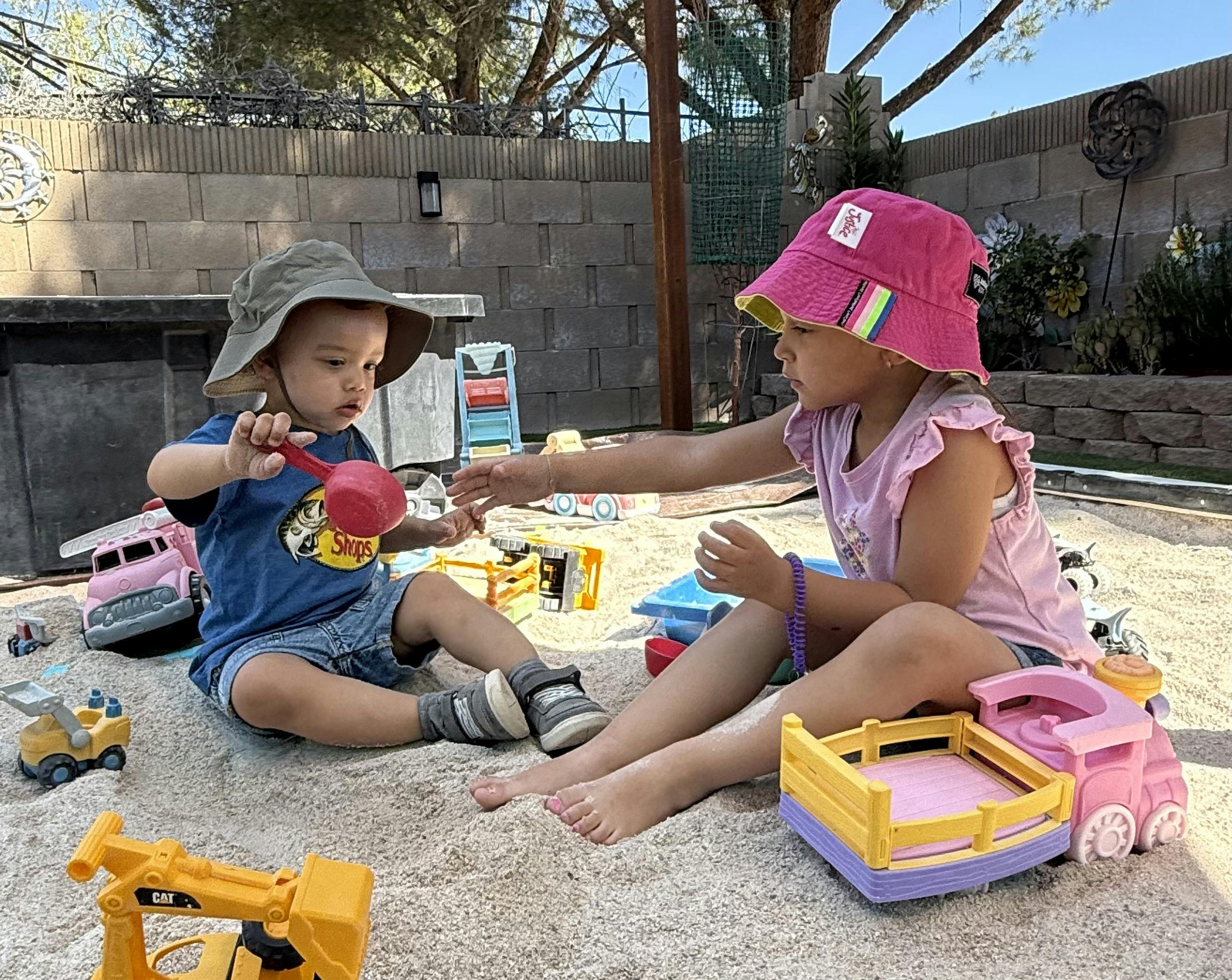 Two children playing in a sandbox with toys
