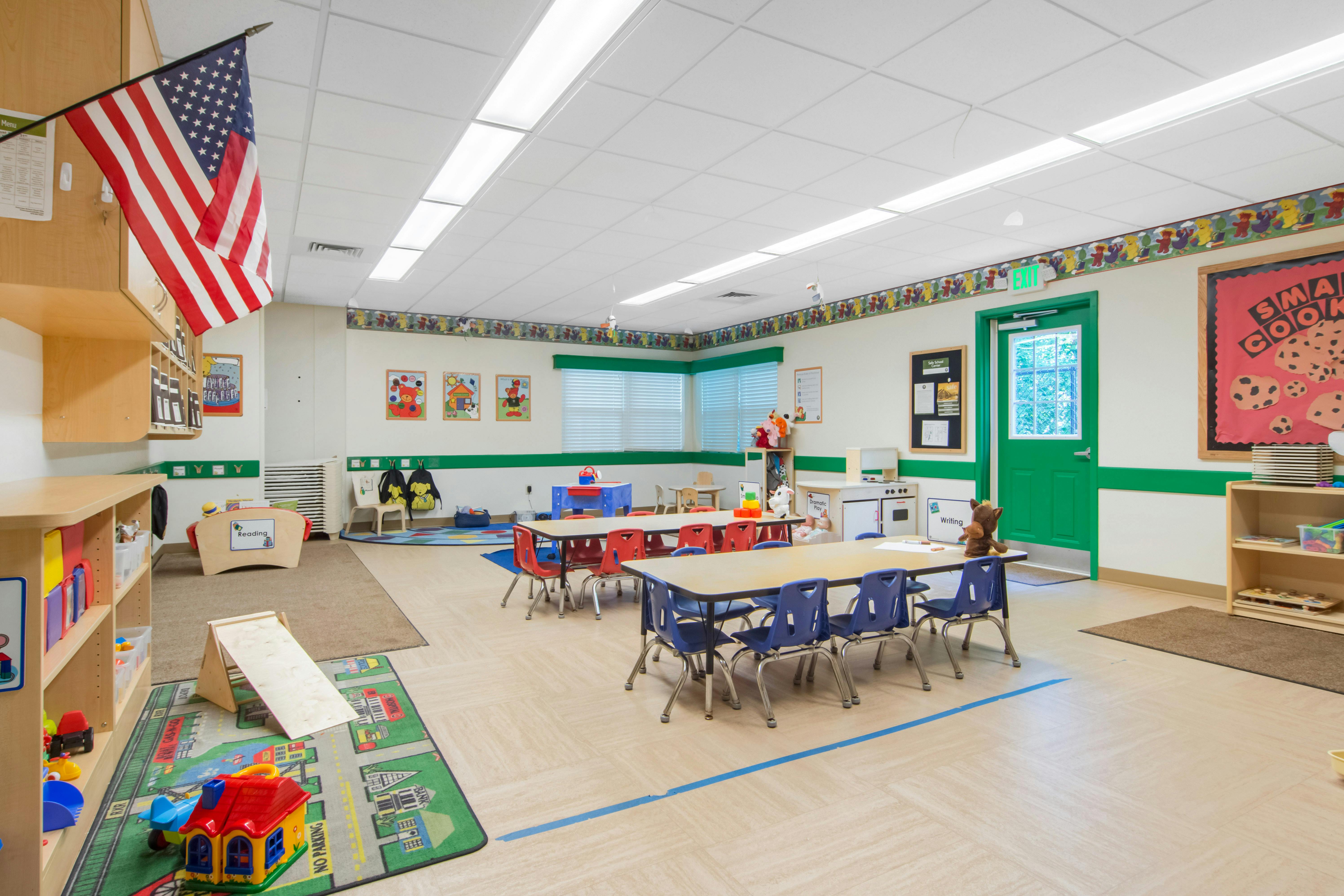 A colorful kindergarten classroom with several tables and chairs, toys, and an American flag