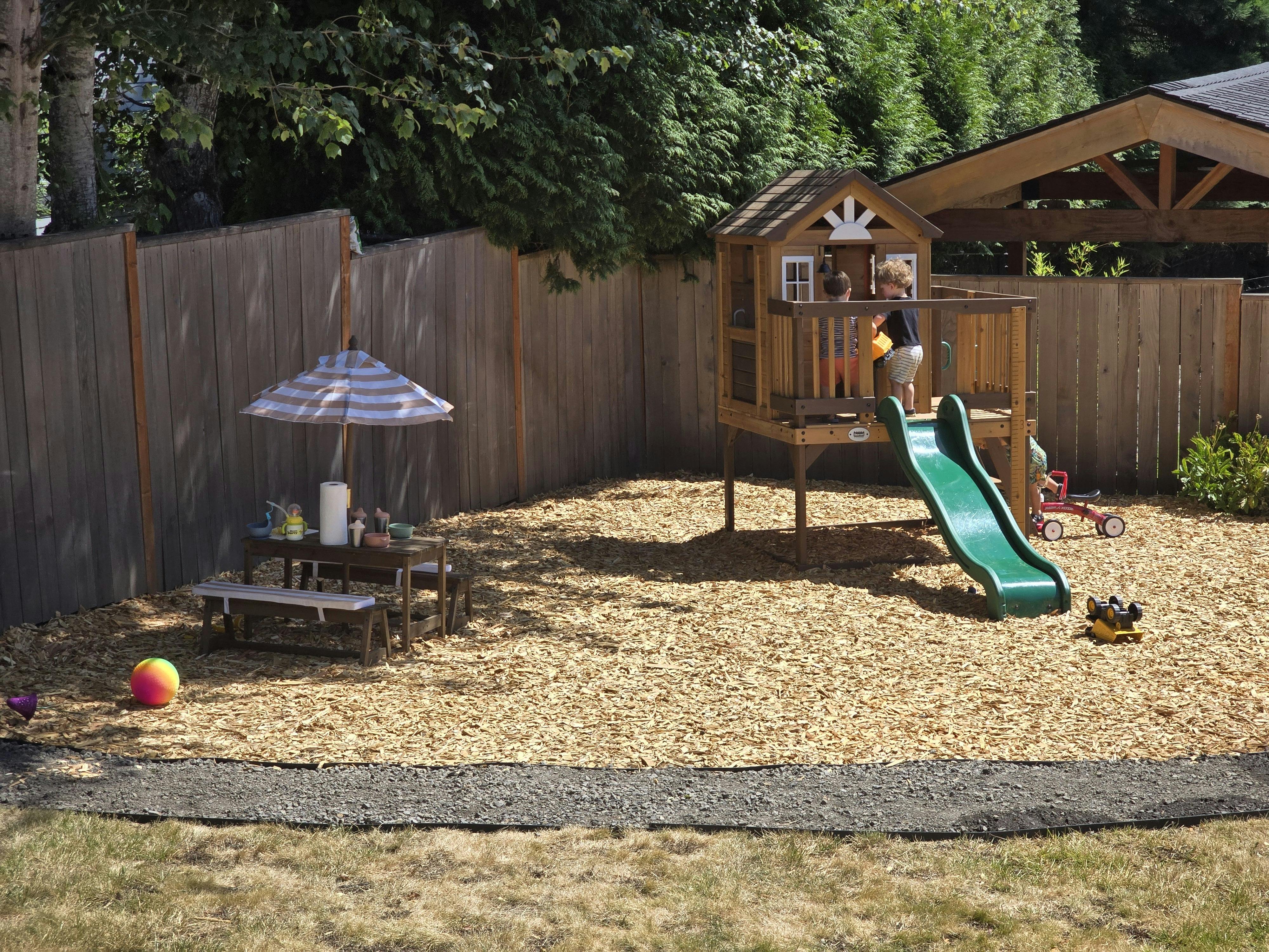 Child on a wooden play structure with a green slide in a backyard