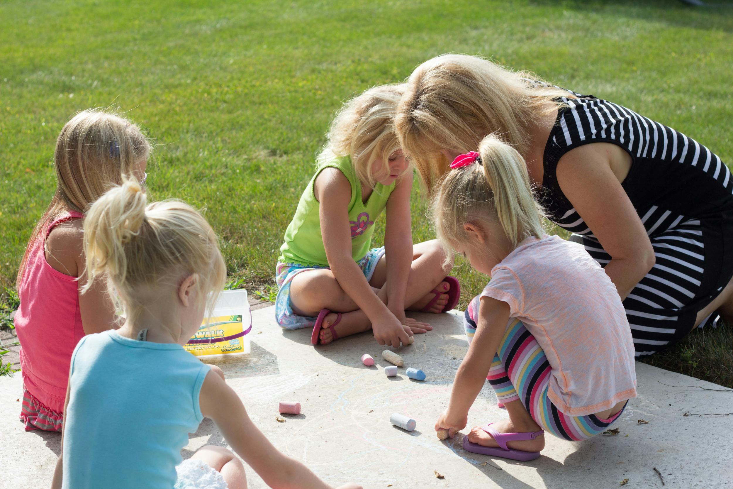Adult and children drawing with chalk on pavement