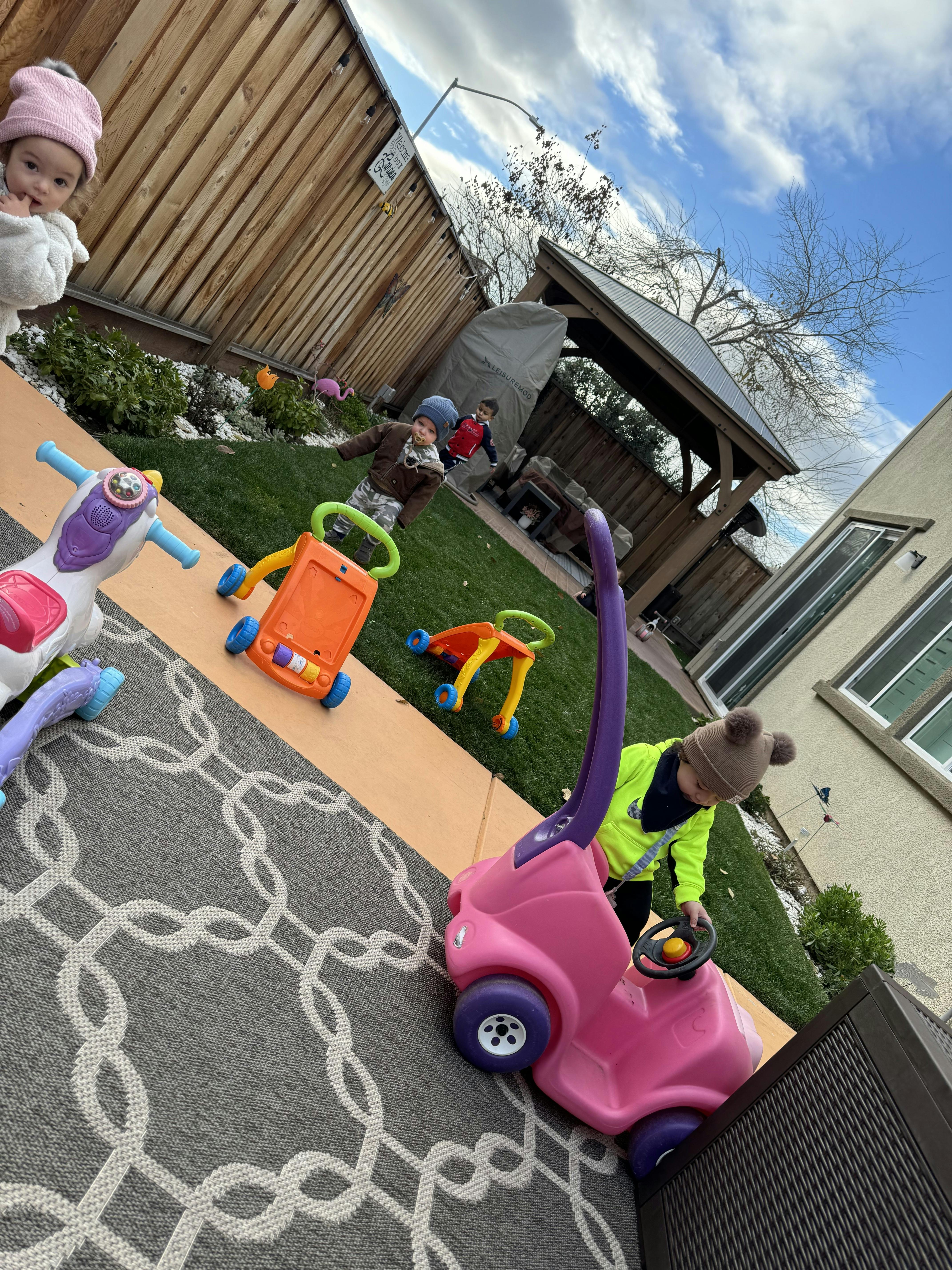 Children playing with toy cars and walkers in a backyard