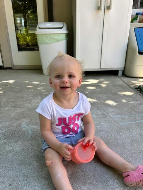 Child sitting on a patio holding a drink cup