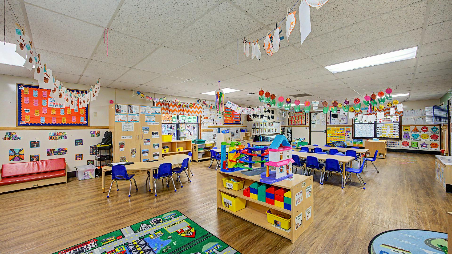 Classroom with small tables and chairs, play area, and student artwork on walls