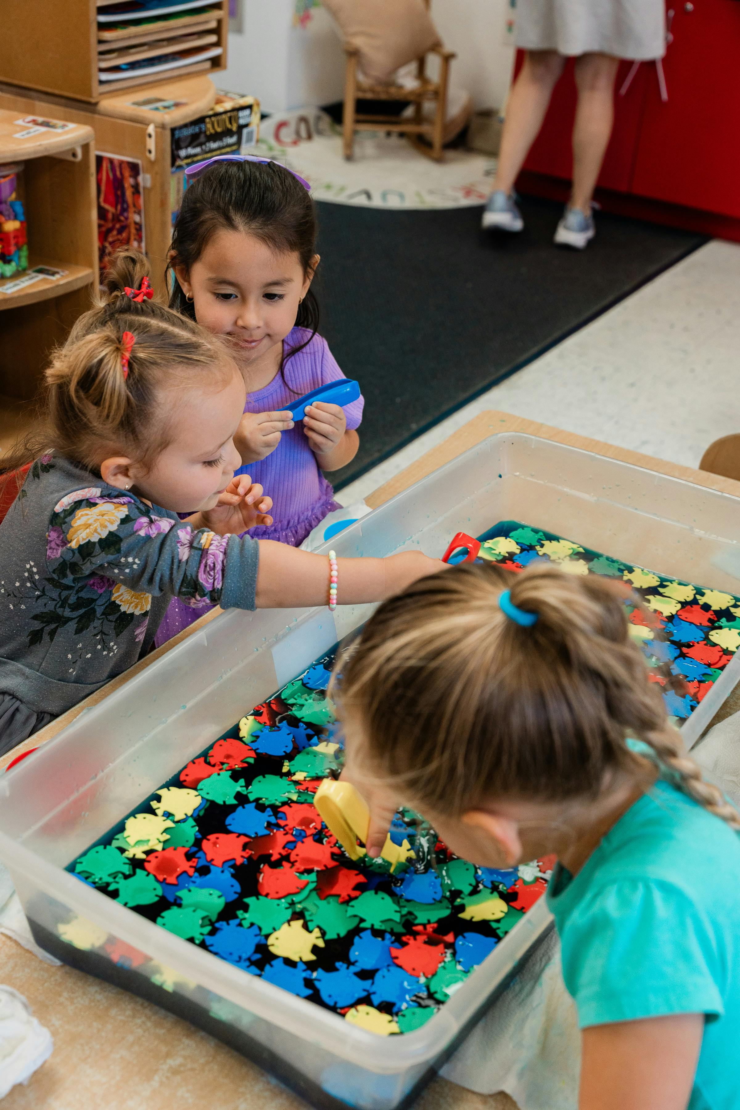 Three children playing with colorful shapes in a clear bin