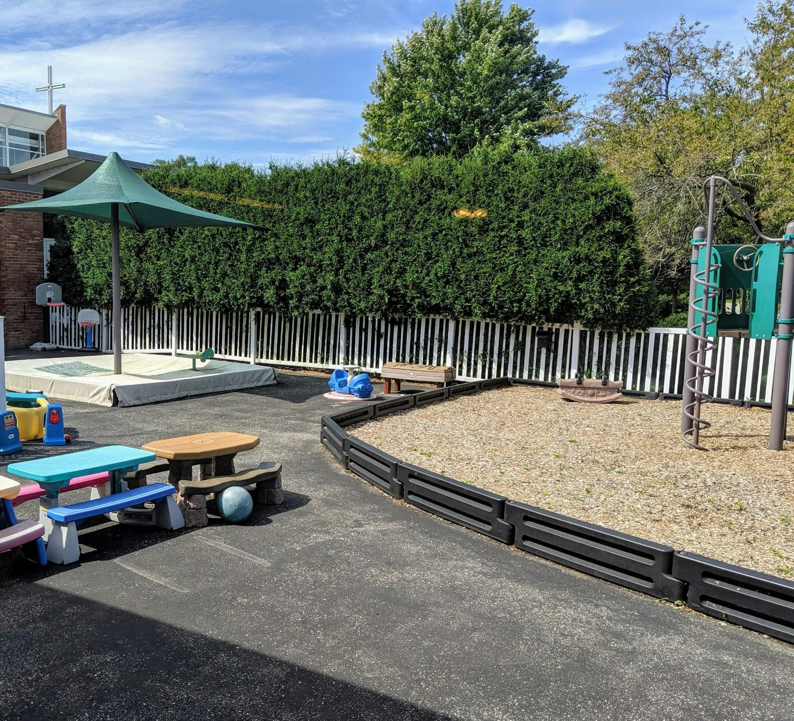 Outdoor playground with sand area, umbrella, and small picnic tables