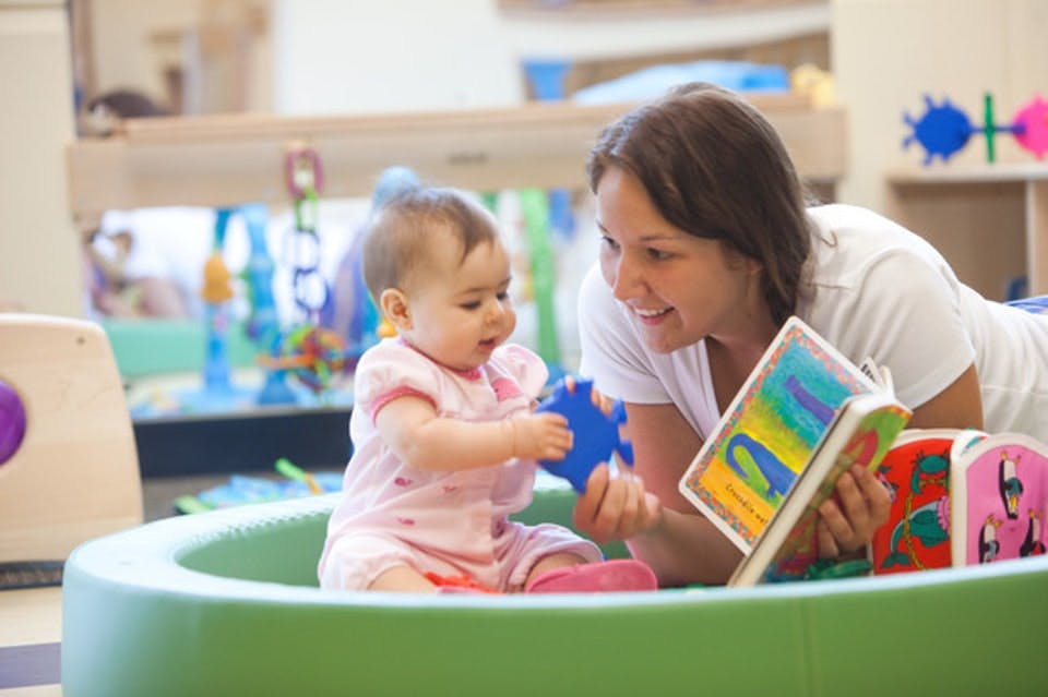 Person reading a book to a child in a play area