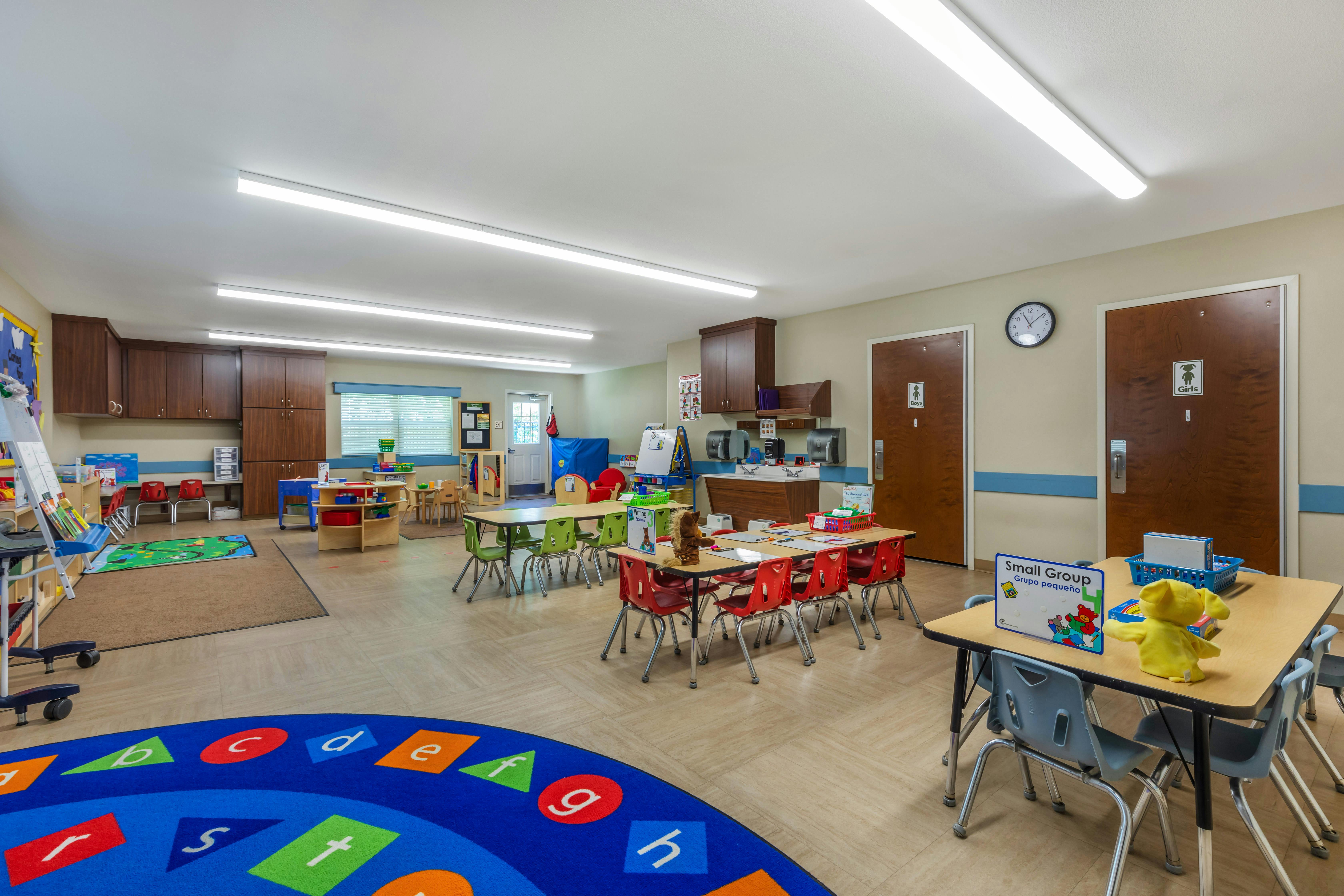 An empty early childhood classroom with small tables, chairs, and colorful rugs