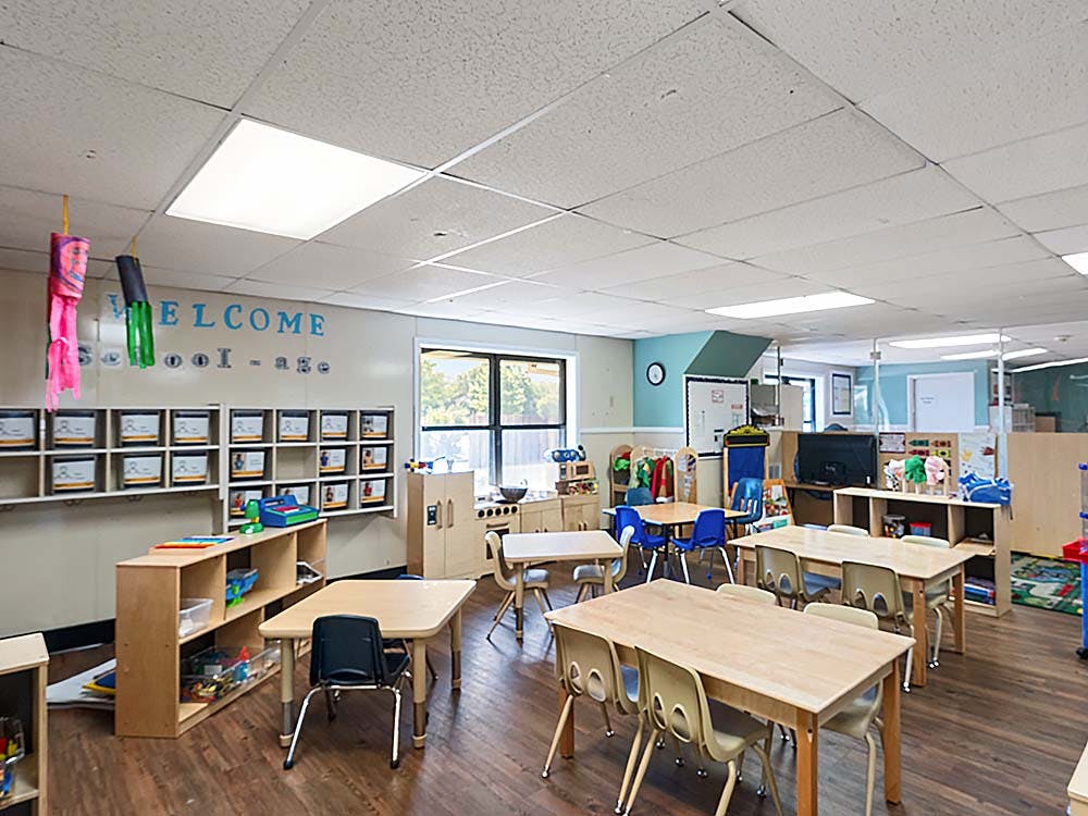 Classroom with small tables and chairs, storage cubbies, and a play kitchen