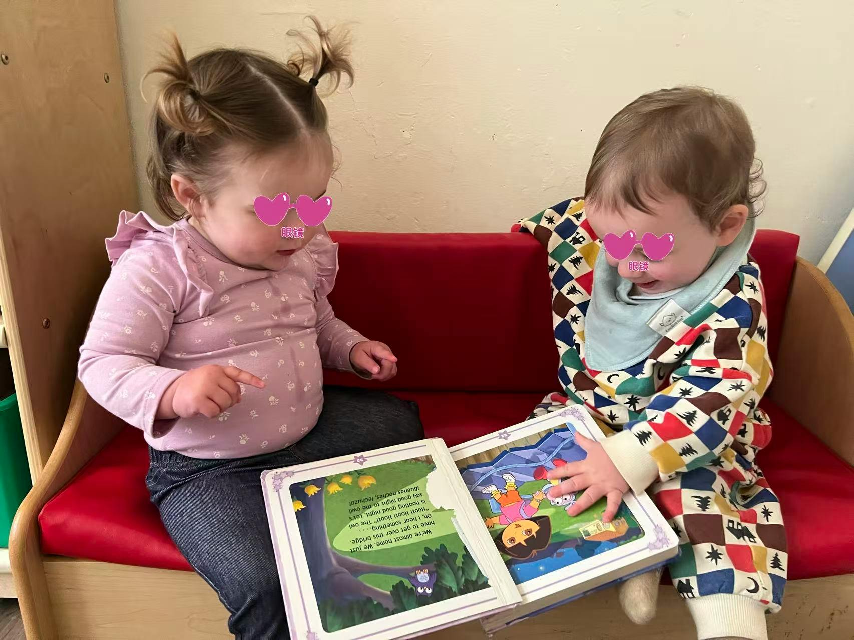 Two children sitting on a red bench, looking at an open book together