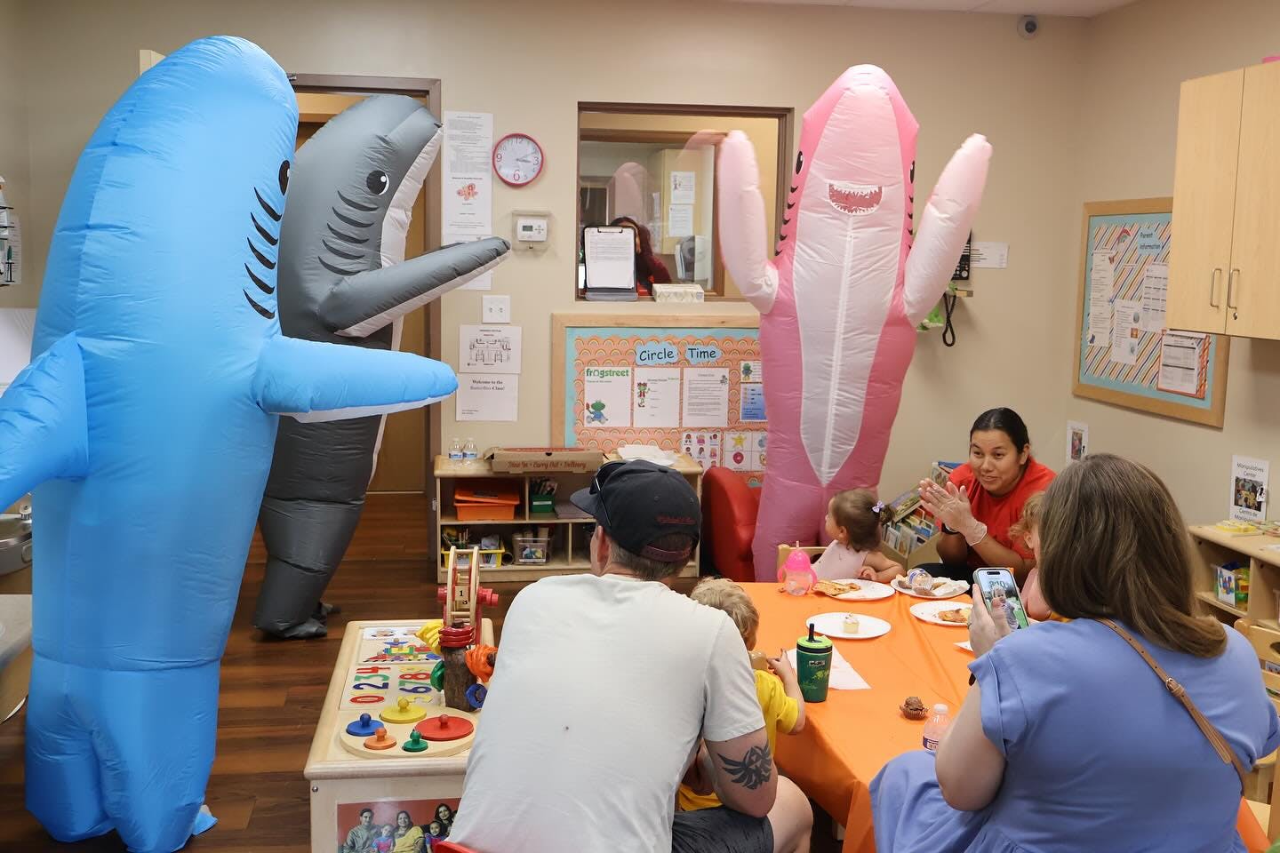 People in shark costumes standing in a classroom with adults and children at a table