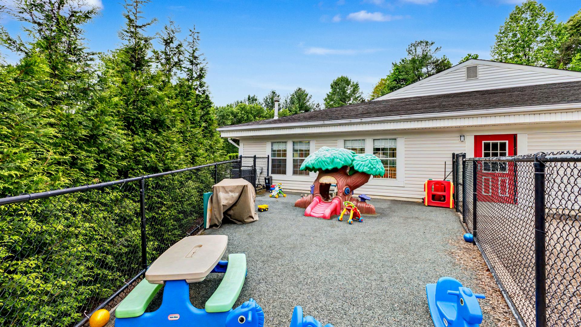 Outdoor playground area with a play structure, slides, and child-sized furniture