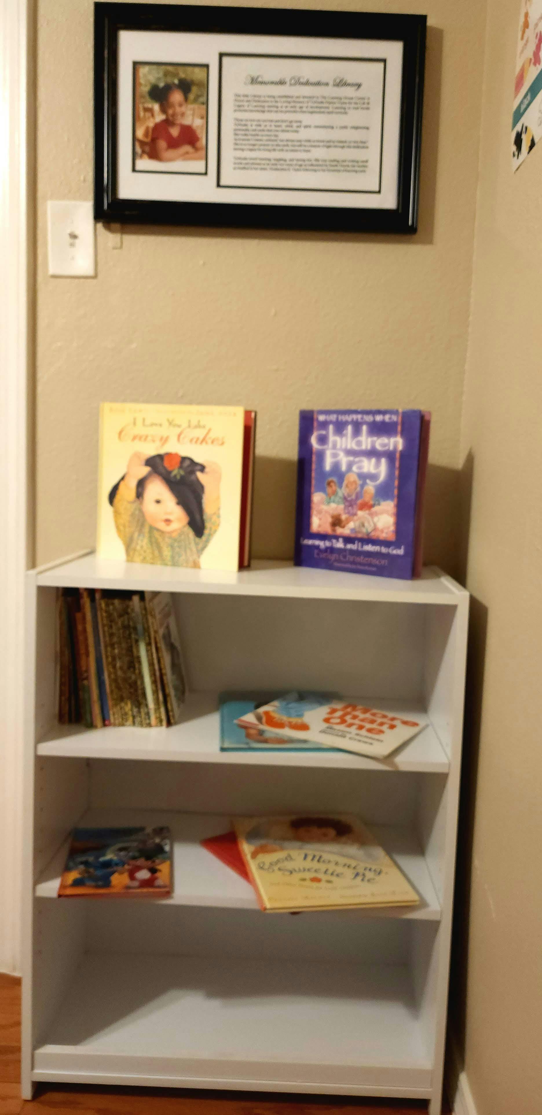 White bookshelf with children's books and a framed picture on the wall