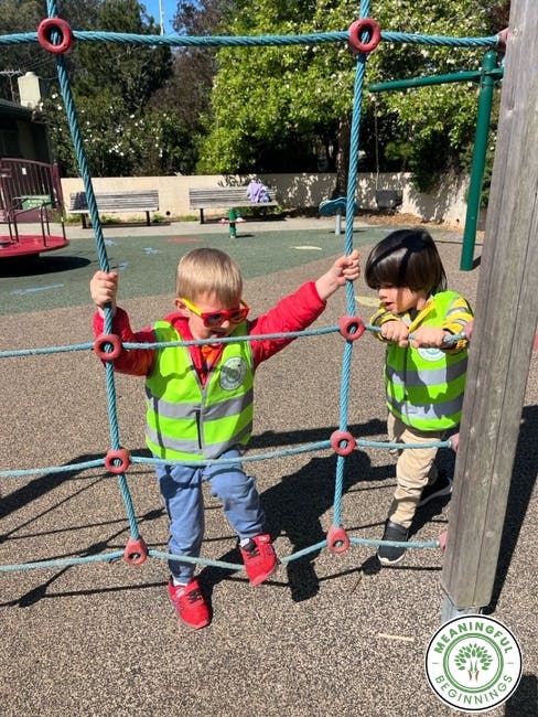 Two children in safety vests playing on rope climbing structure