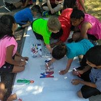Children drawing on a large sheet of paper outdoors