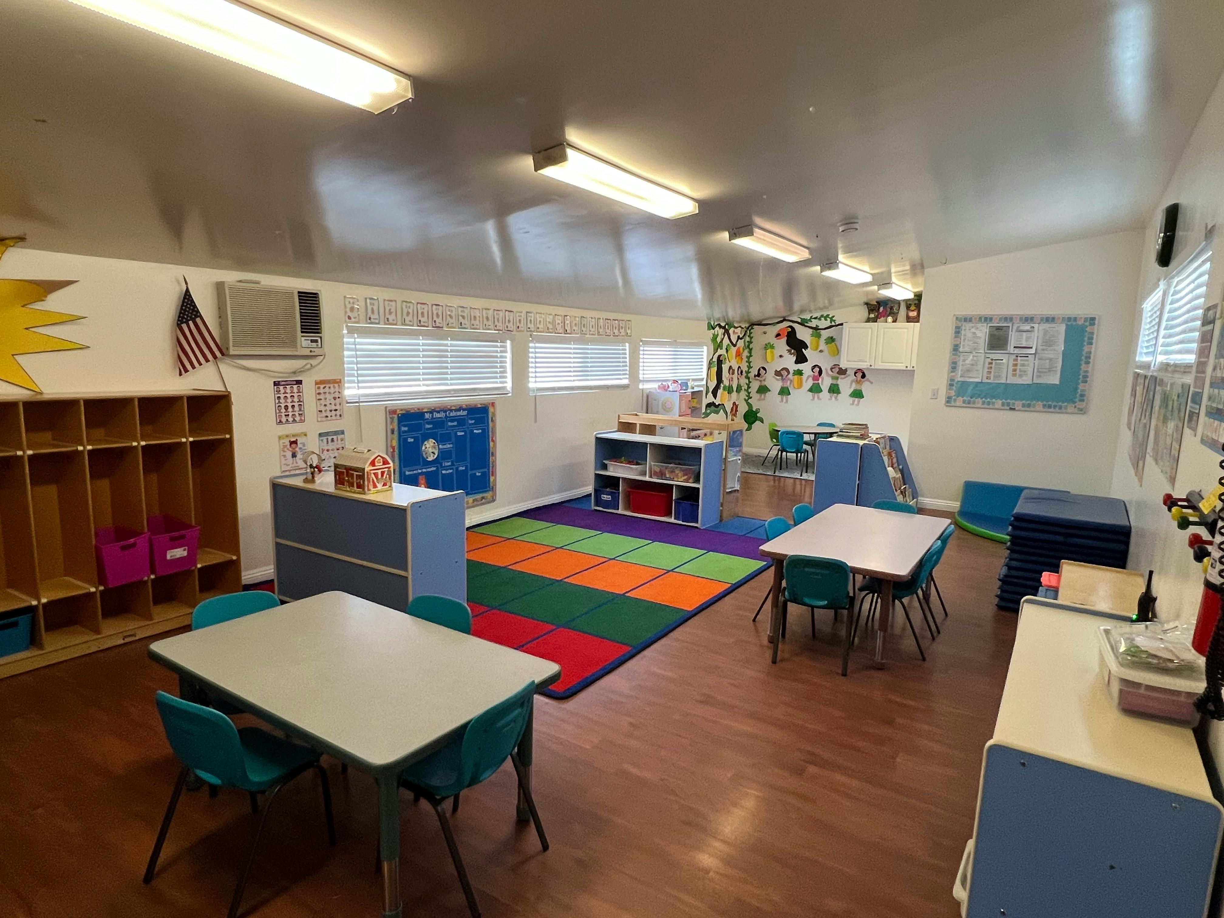 Empty classroom with small tables and chairs, cubbies, and a colorful rug