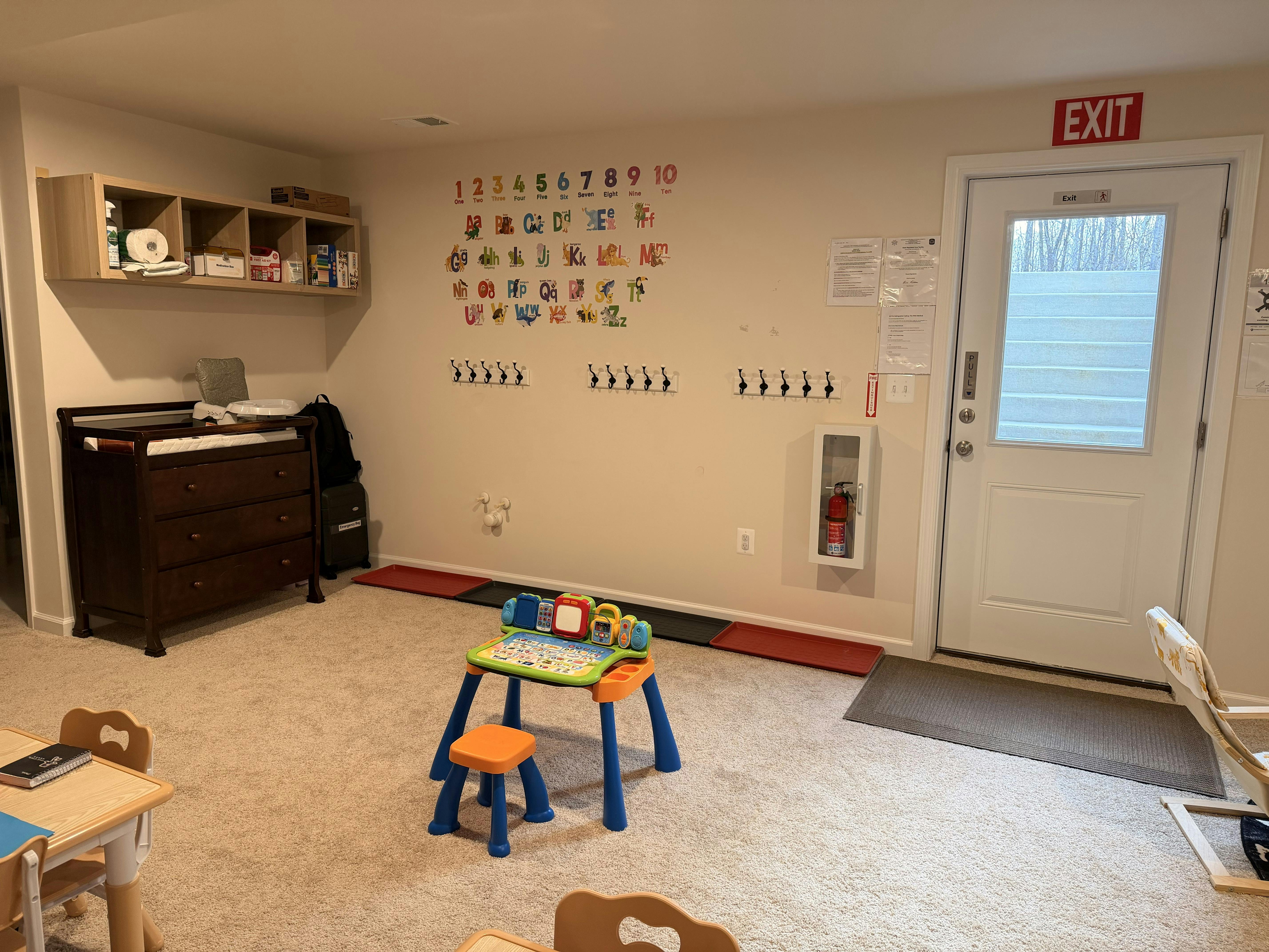 Childcare room with a changing table, small play table, and alphabet wall stickers