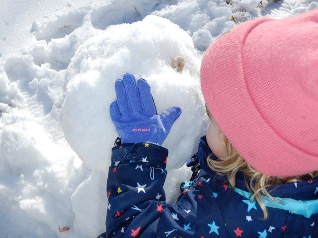 Child in winter clothing touching a snowman