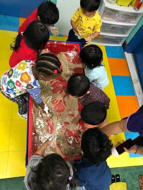 Children playing with sand and red paint in a sensory bin