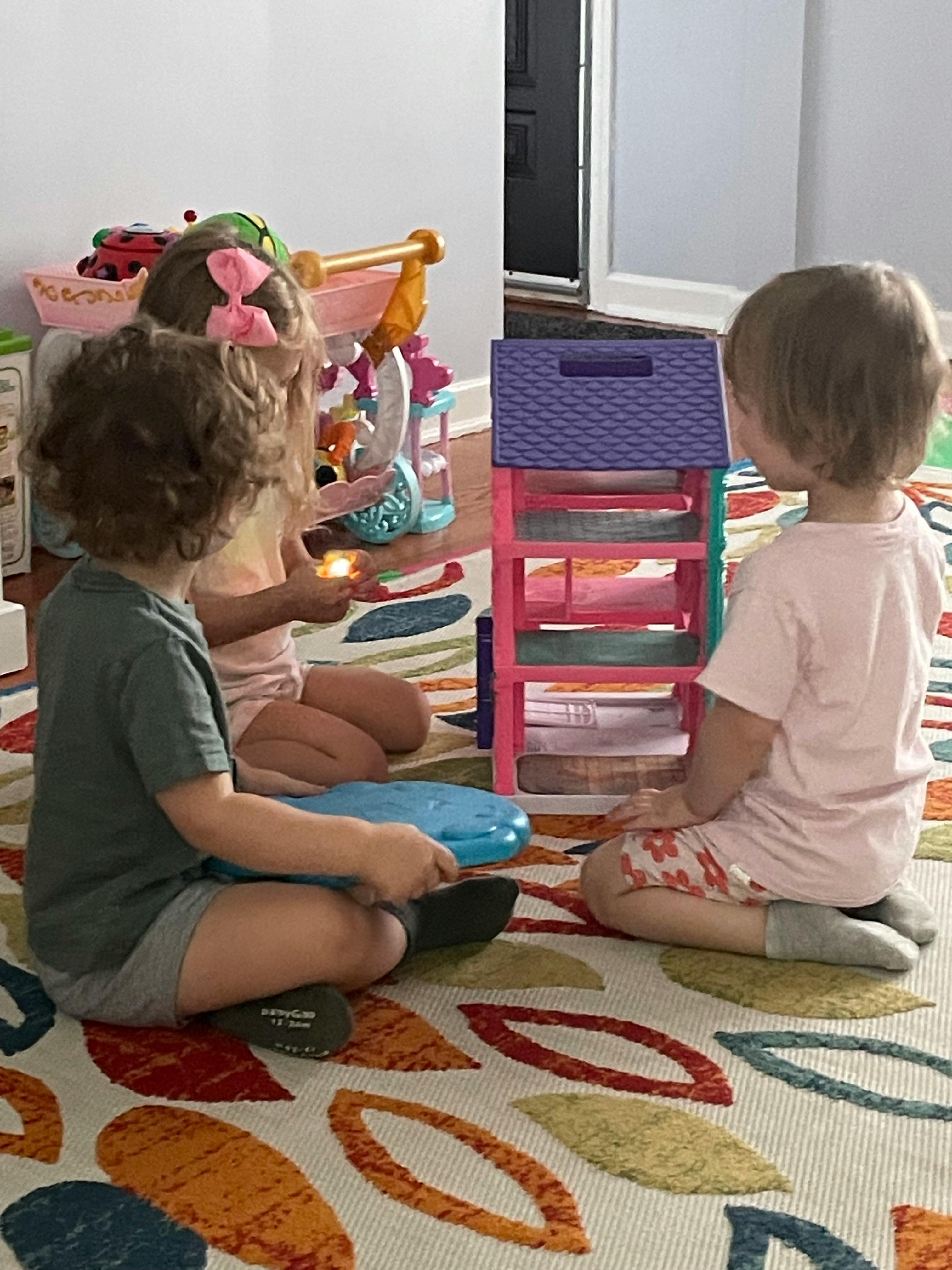 Three children playing on a rug with toys