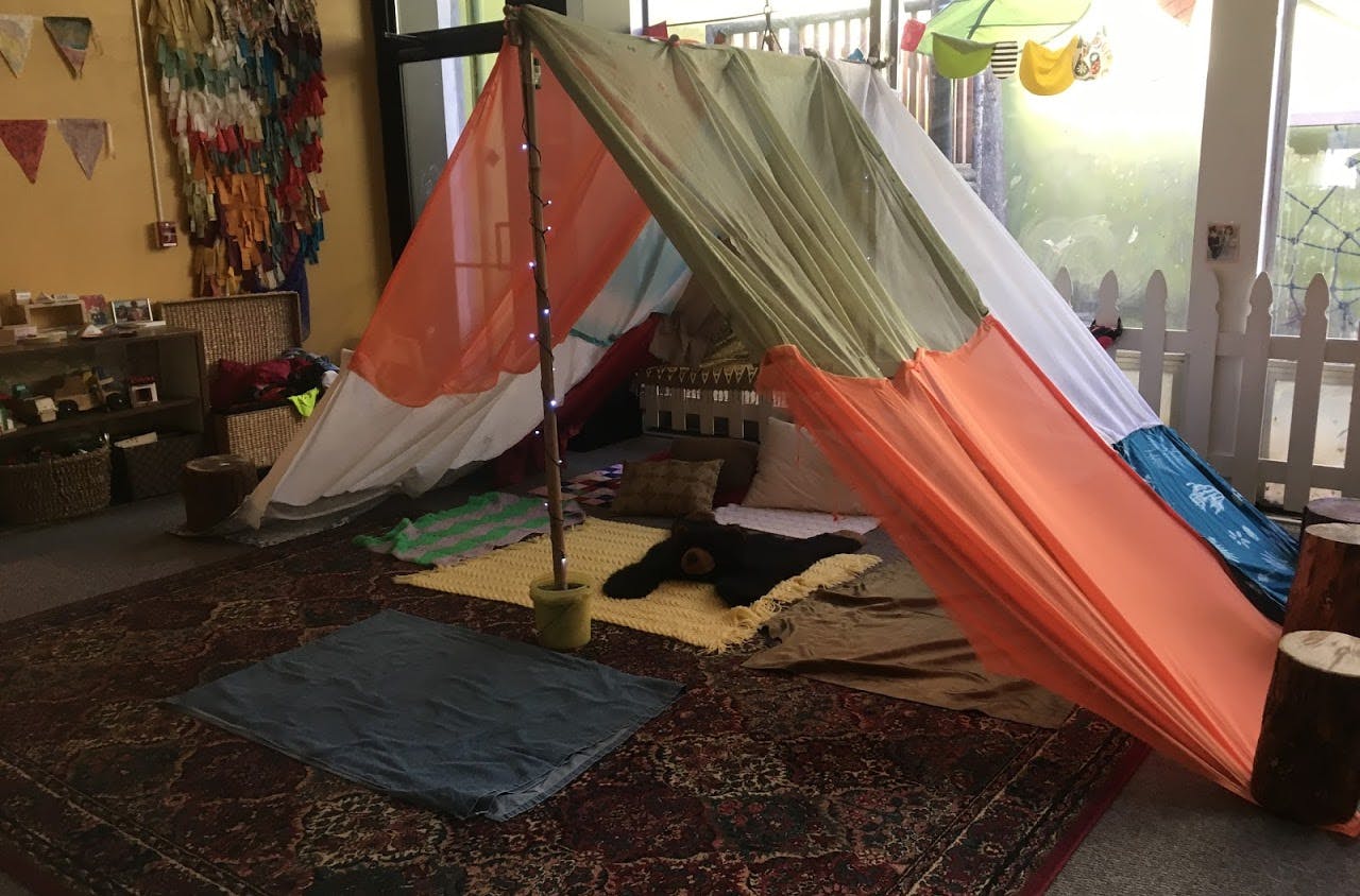 Indoor fort made from colorful fabric sheets over a pole with blankets on the floor