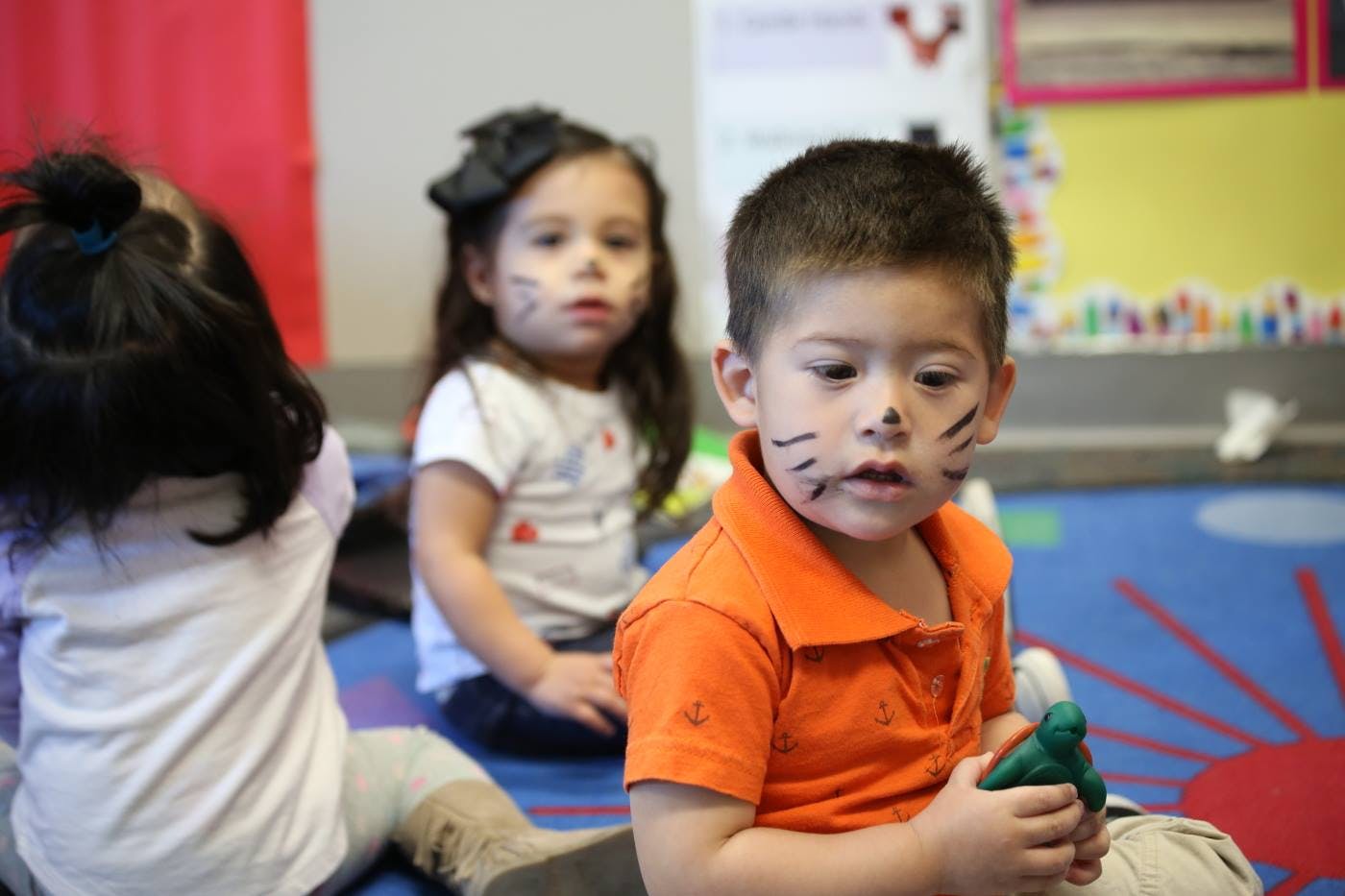 Three children with face paint sitting on a floor