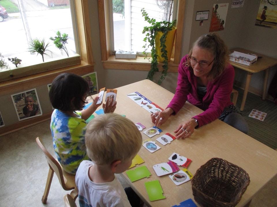 Adult and two children at a table with cards in a classroom playing a card game