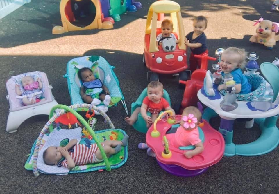 Multiple babies playing in various seats and on a play mat outdoors