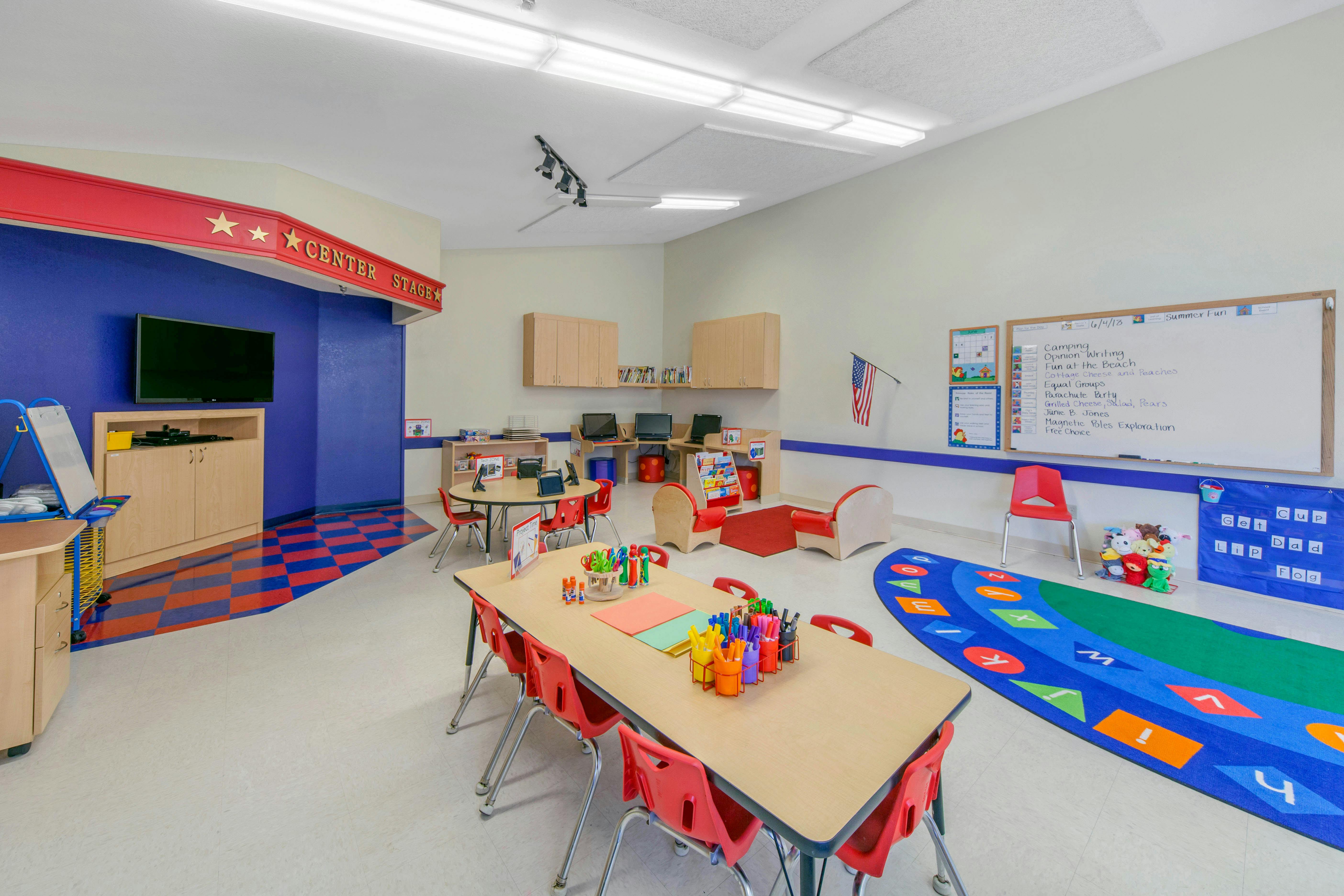 Classroom with tables, chairs, computers, and a whiteboard listing activities