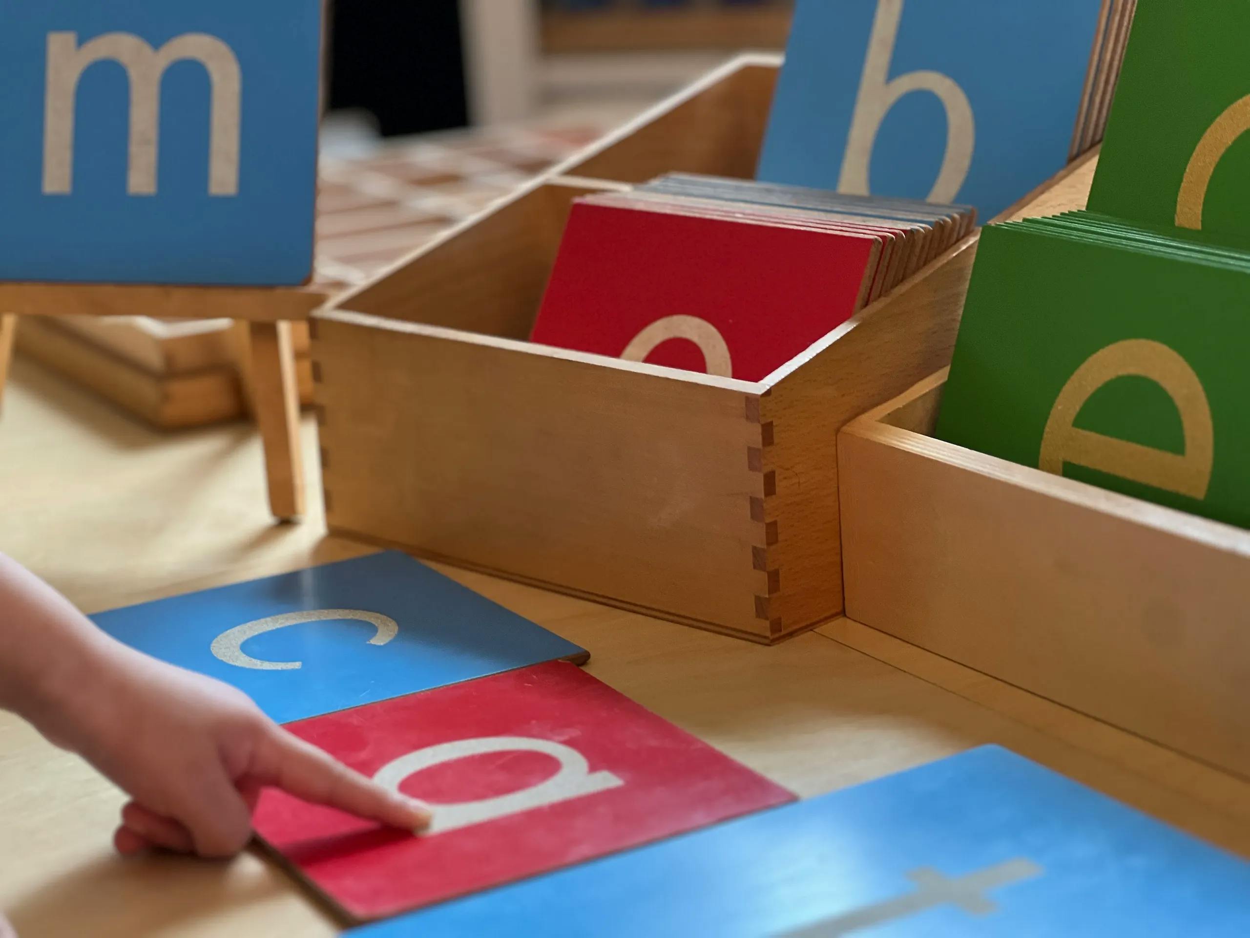 Child's hand pointing to a letter 'a' on a learning card