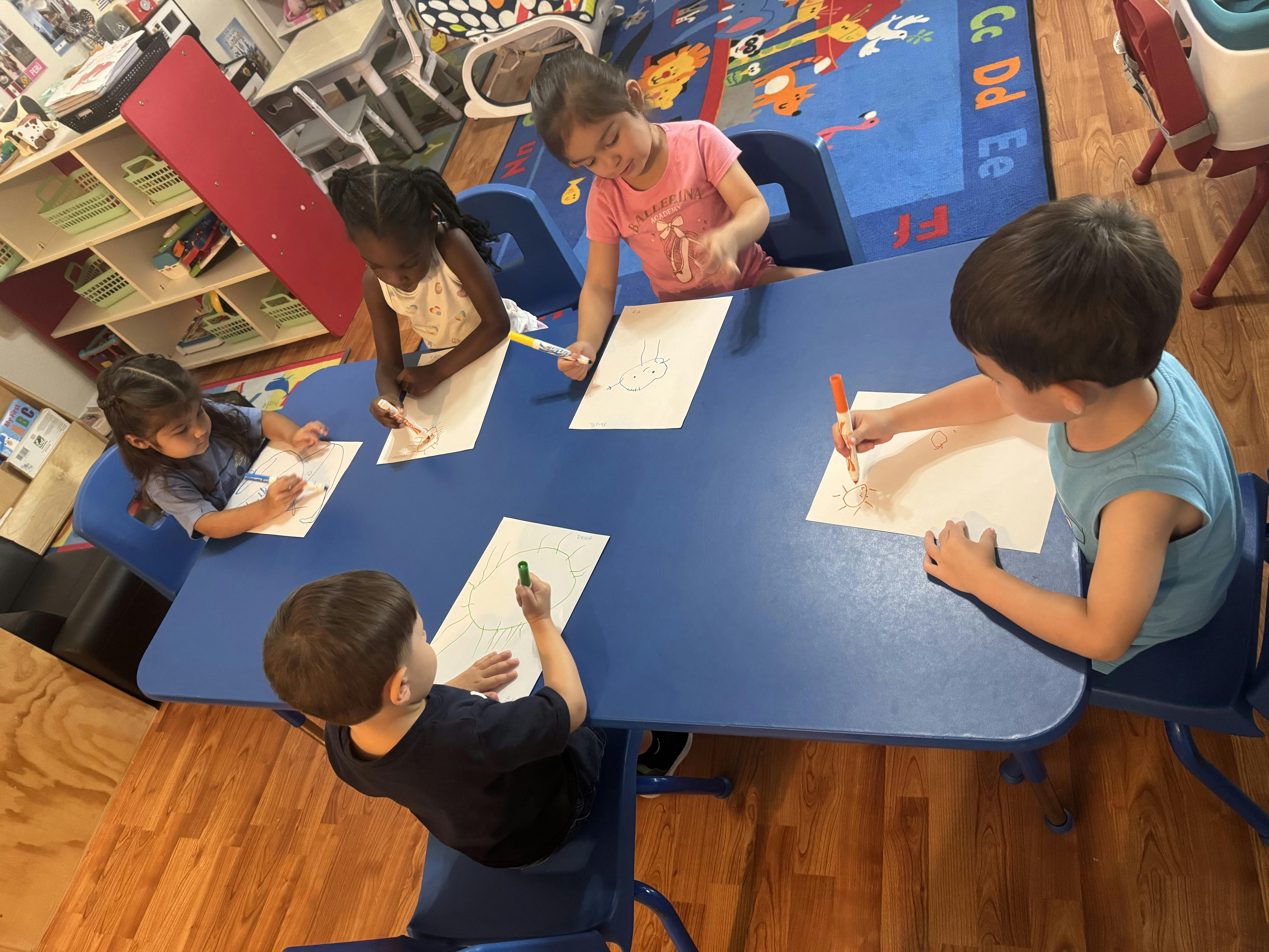 Children drawing at a blue table in a classroom